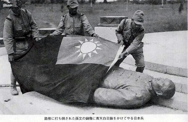 孙中山先生的铜像倒在路旁，几个日本强盗假惺惺的给铜像盖上一面青天白日旗。 