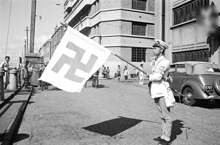 街头穿制服的男子举着红卍字旗帜。臂带卍标志的人可能是一个红卍字会中心的成员，该组织向战争受害者提供救济服务。这不是纳粹标志（图案相反）。1937年。